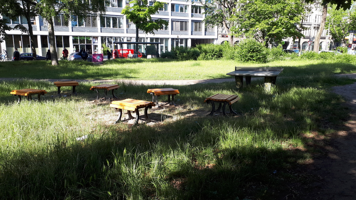 hölzerne Sitzmöbel und feste Tischtennisplatte im Sonnenlicht auf der Grünfläche Ecke Moritzplatz