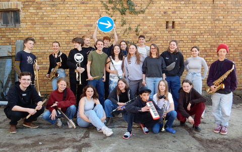 eine Gruppe junger Menschen mit Instrumenten posiert vor einer Mauer