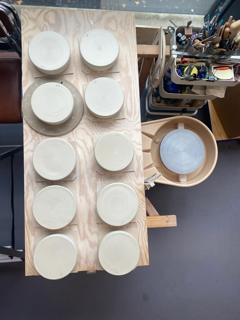 zwölf gedrehte Tonscheiben von oben fotografiert auf einem Tisch in zwei Reihen